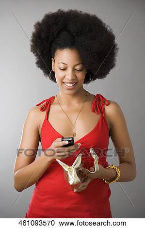 Stock Image - Close-up of a young woman using a mobile phone and holding a purse. Fotosearch