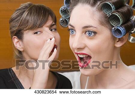 Close-up of a young woman whispering into the ear of another young woman View Large Photo Image Picture - Close-up of a young woman whispering into the ear of another young woman. Fotosearch