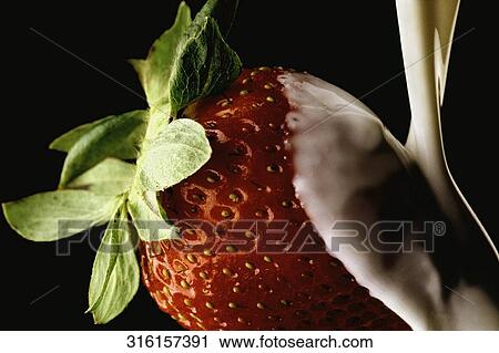 Stock Image - Close-up of cream being poured on a strawberry. Fotosearch