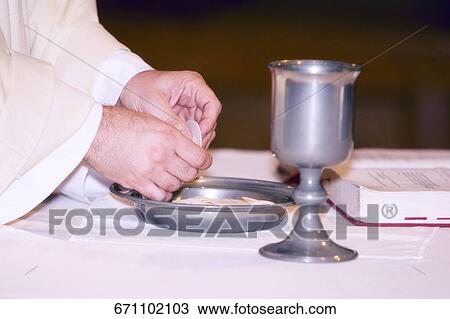 Stock Image - Close-up of hands of a priest breaking bread. Fotosearch