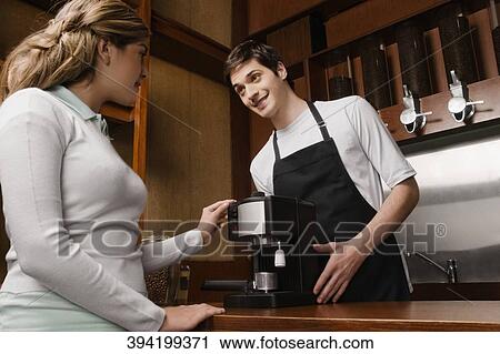 Stock Image - Coffee shop owner showing a coffee maker to a customer. Fotosearch