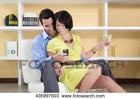 Stock Image - Couple sitting on a chair and looking at a mobile phone. Fotosearch