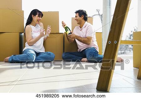 Stock Photography - Couple sitting on the floor and celebrating with champagne. Fotosearch