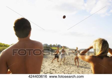 Stock Photograph - Five friends playing American football on the beach. Fotosearch