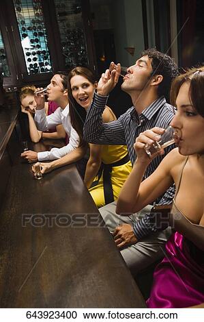 Stock Image - Five friends sitting at a bar counter and drinking whiskey. Fotosearch