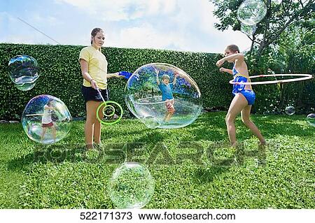 Stock Image - Four friends playing with bubbles and plastic hoop. Fotosearch