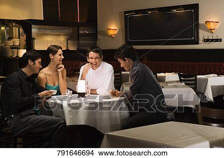 Four friends sitting at a table in a restaurant and smiling View Large Photo Image Picture - Four friends sitting at a table in a restaurant and smiling. Fotosearch