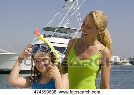 Stock Photo - Girl holding a snorkel and standing with her mother. Fotosearch