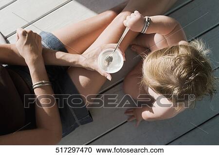 High angle view of a baby girl dipping a spoon in a cup held by her mother View Large Photo Image Stock Image - High angle view of a baby girl dipping a spoon in a cup held by her mother. Fotosearch