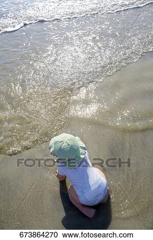 High angle view of a baby girl kneeling on the beach View Large Photo Image Stock Image - High angle view of a baby girl kneeling on the beach. Fotosearch