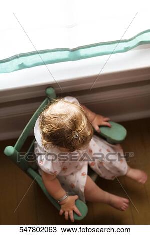 Stock Image - High angle view of a baby girl sitting in an armchair. Fotosearch