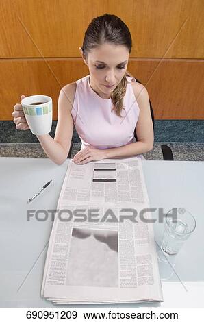 High angle view of a businesswoman holding a coffee cup and reading a newspaper View Large Photo Image Stock Photo - High angle view of a businesswoman holding a coffee cup and reading a newspaper. Fotosearch