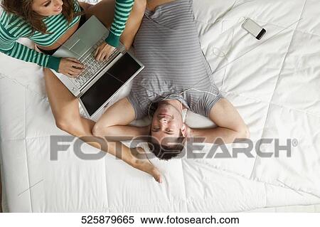 High angle view of a mid adult man listening to an MP3 player with a young woman using a laptop View Large Photo Image Stock Photography - High angle view of a mid adult man listening to an MP3 player with a young woman using a laptop. Fotosearch