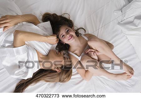 Stock Image - High angle view of a mid adult woman lying on the bed with her daughter. Fotosearch