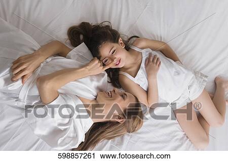 Stock Image - High angle view of a mid adult woman lying on the bed with her daughter. Fotosearch