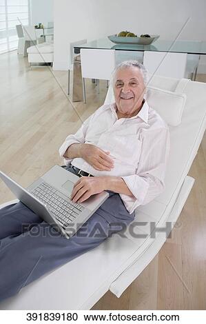 High angle view of a senior man using a laptop and smiling View Large Photo Image Stock Image - High angle view of a senior man using a laptop and smiling. Fotosearch