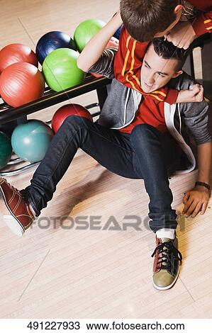 Stock Image - High angle view of a young man gripping another young man's neck in a bowling alley. Fotosearch