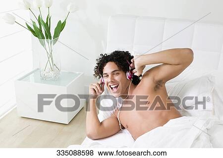 High angle view of a young man lying on the bed and listening to music View Large Photo Image Stock Photo - High angle view of a young man lying on the bed and listening to music. Fotosearch