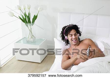 High angle view of a young man lying on the bed and listening to music View Large Photo Image Stock Photo - High angle view of a young man lying on the bed and listening to music. Fotosearch