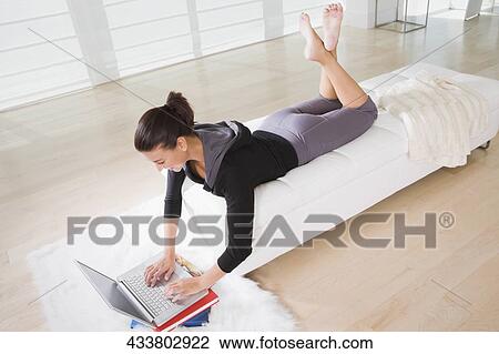 High angle view of a young woman lying on the bed and using a laptop View Large Photo Image Stock Image - High angle view of a young woman lying on the bed and using a laptop. Fotosearch