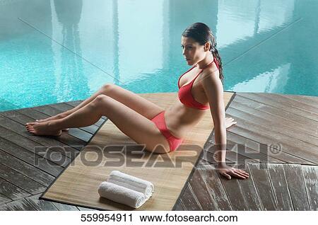 Stock Image - High angle view of a young woman sitting at the poolside. Fotosearch