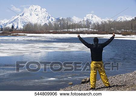 Hiker standing at the lakeside with snow covered mountains in the background, Grand Teton National Park, Wyoming, USA View Large Photo Image Stock Photograph - Hiker standing at the lakeside with snow covered mountains in the background, Grand Teton National Park, Wyoming, USA. Fotosearch