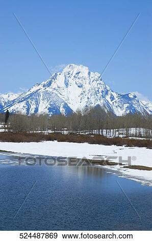 Stock Photo - Lake with a snow covered mountain in the background, Grand Teton National Park, Wyoming, USA. Fotosearch