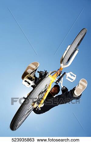 Stock Image - Low angle view of a BMX cyclist performing in mid-air. Fotosearch