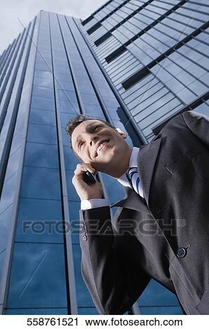 Low angle view of a businessman talking on a mobile phone and smiling View Large Photo Image Stock Image - Low angle view of a businessman talking on a mobile phone and smiling. Fotosearch