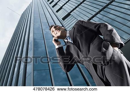Low angle view of a businessman talking on a mobile phone and smiling View Large Photo Image Stock Photograph - Low angle view of a businessman talking on a mobile phone and smiling. Fotosearch