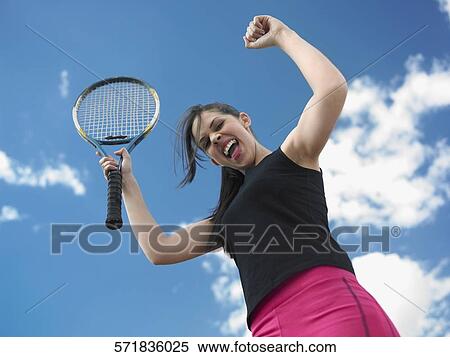 Stock Photography - Low angle view of a female tennis player holding a tennis racket with her hands raised. Fotosearch