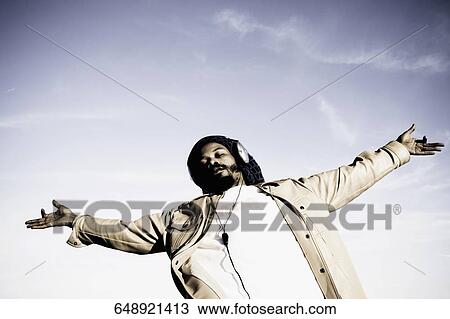 Low angle view of a mid adult man listening to music with his arms outstretched View Large Photo Image Stock Image - Low angle view of a mid adult man listening to music with his arms outstretched. Fotosearch