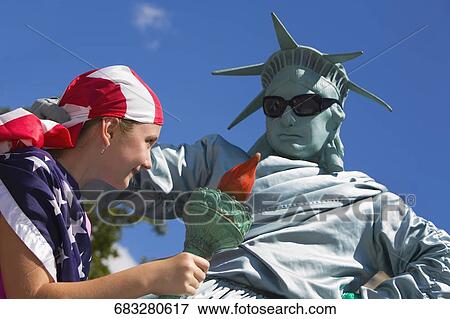 Low angle view of a mid adult man dresses as the Statue of Liberty with a girl holding a flaming torch beside him, New York City, New York State, USA View Large Photo Image Stock Photo - Low angle view of a mid adult man dresses as the Statue of Liberty with a girl holding a flaming torch beside him, New York City, New York State, USA. Fotosearch