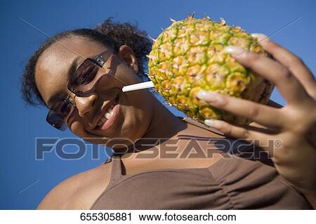Stock Image - Low angle view of a teenage girl holding a pineapple cocktail, Chicago, Illinois. Fotosearch