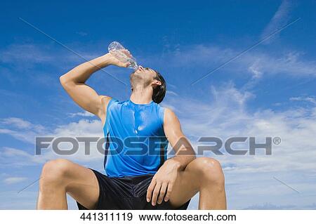 Low angle view of a young man drinking water from a water bottle View Large Photo Image Stock Photo - Low angle view of a young man drinking water from a water bottle. Fotosearch