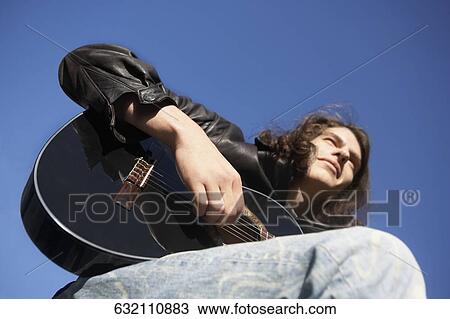 Low angle view of a young man playing the guitar View Large Photo Image Stock Image - Low angle view of a young man playing the guitar. Fotosearch