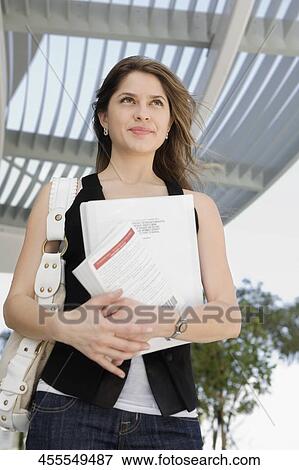 Low angle view of a young woman holding a textbook View Large Photo Image Stock Photo - Low angle view of a young woman holding a textbook. Fotosearch