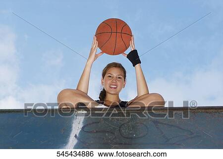 Low angle view of a young woman holding a basketball View Large Photo Image Stock Photograph - Low angle view of a young woman holding a basketball. Fotosearch