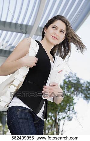 Low angle view of a young woman holding a textbook View Large Photo Image Stock Photography - Low angle view of a young woman holding a textbook. Fotosearch