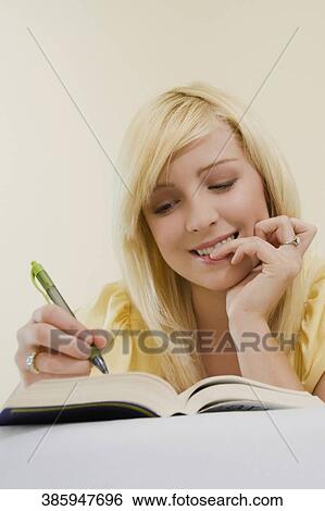 Stock Photograph - Low angle view of a young woman lying on the bed and writing with a pen in a book. Fotosearch