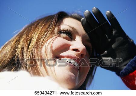 Low angle view of a young woman shielding her eyes View Large Photo Image Stock Image - Low angle view of a young woman shielding her eyes. Fotosearch