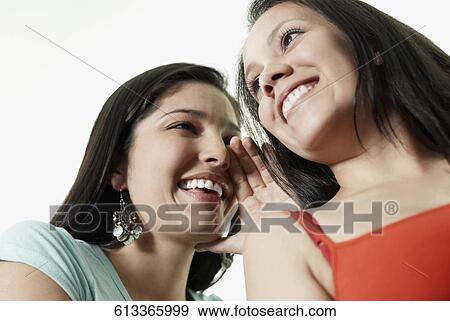 Stock Photo - Low angle view of a young woman whispering to another young woman. Fotosearch