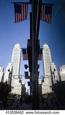 Stock Image - Low angle view of American flags hanging on poles with skyscrapers in the background, New York City, New York State, USA. Fotosearch