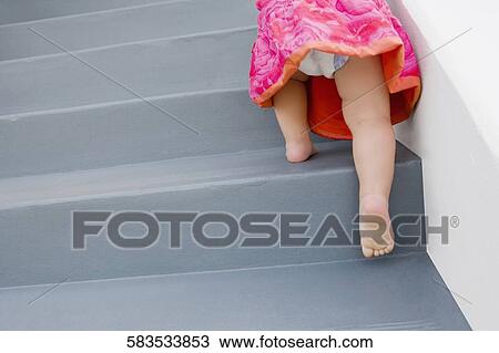 Stock Image - Low section view of a baby girl climbing up staircase. Fotosearch