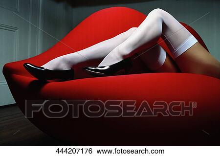 Stock Photograph - Low section view of a woman lying on a red couch. Fotosearch