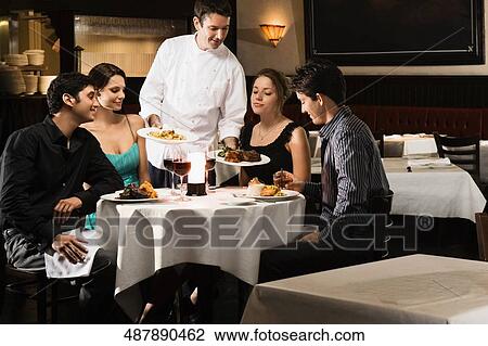 Male chef serving food to two young couples sitting in a restaurant View Large Photo Image Stock Image - Male chef serving food to two young couples sitting in a restaurant. Fotosearch