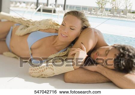 Stock Photograph - Mid adult couple resting at poolside. Fotosearch