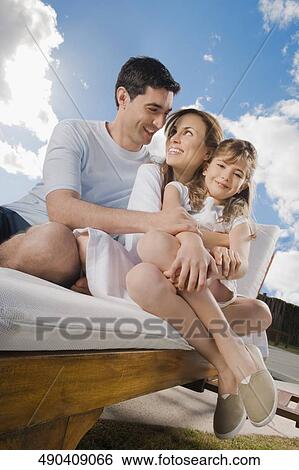 Mid adult couple sitting with their daughter on a reclining chair View Large Photo Image Stock Photograph - Mid adult couple sitting with their daughter on a reclining chair. Fotosearch