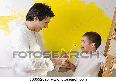 Stock Photograph - Mid adult man and his son playing with paint rollers and smiling. Fotosearch