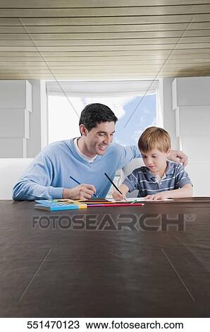 Stock Image - Mid adult man assisting his son in his homework. Fotosearch